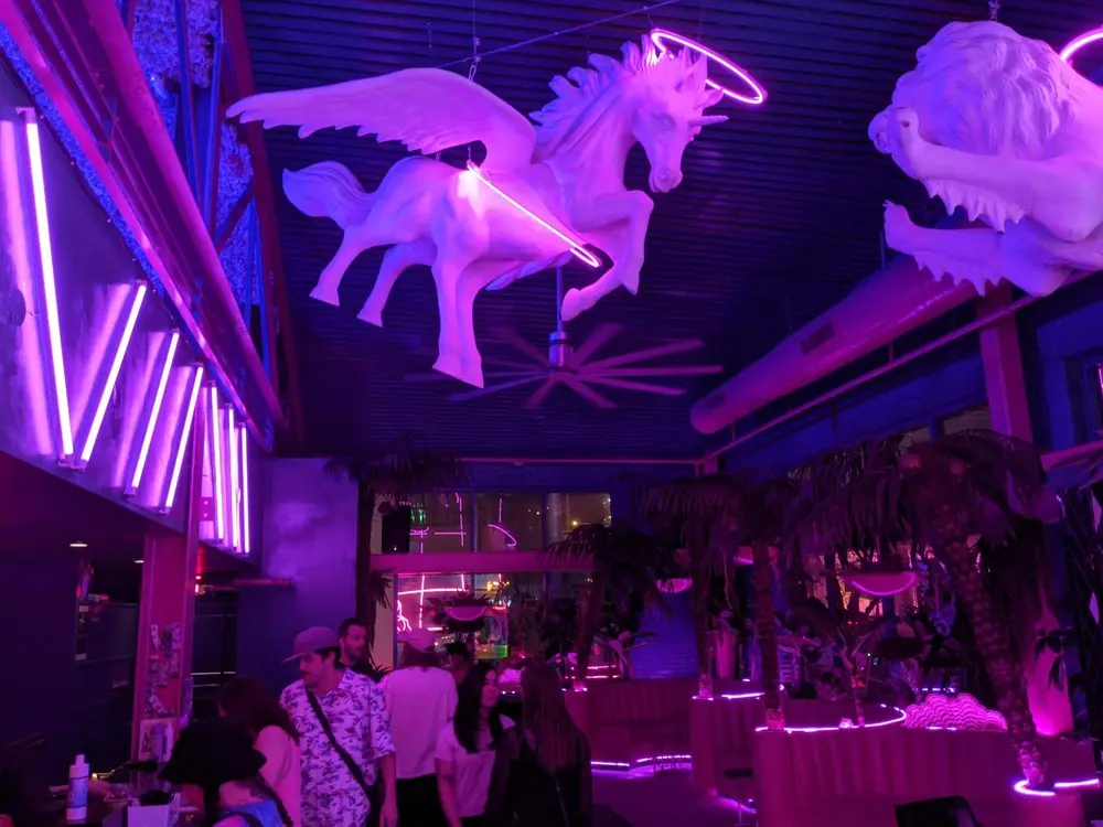 Pegasus sculpture over palms and glowing pink booths