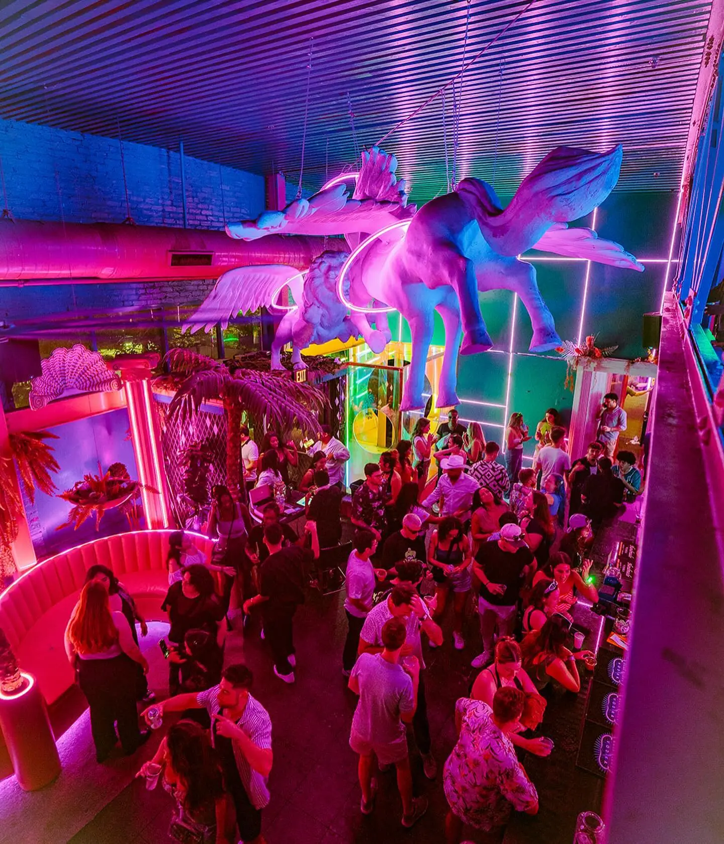 Crowd under the glowing pink pegasus and winged lion sculptures inside Neon Grotto