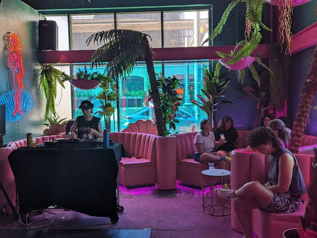 DJ playing beside the neon Venus sign and pink curved booths