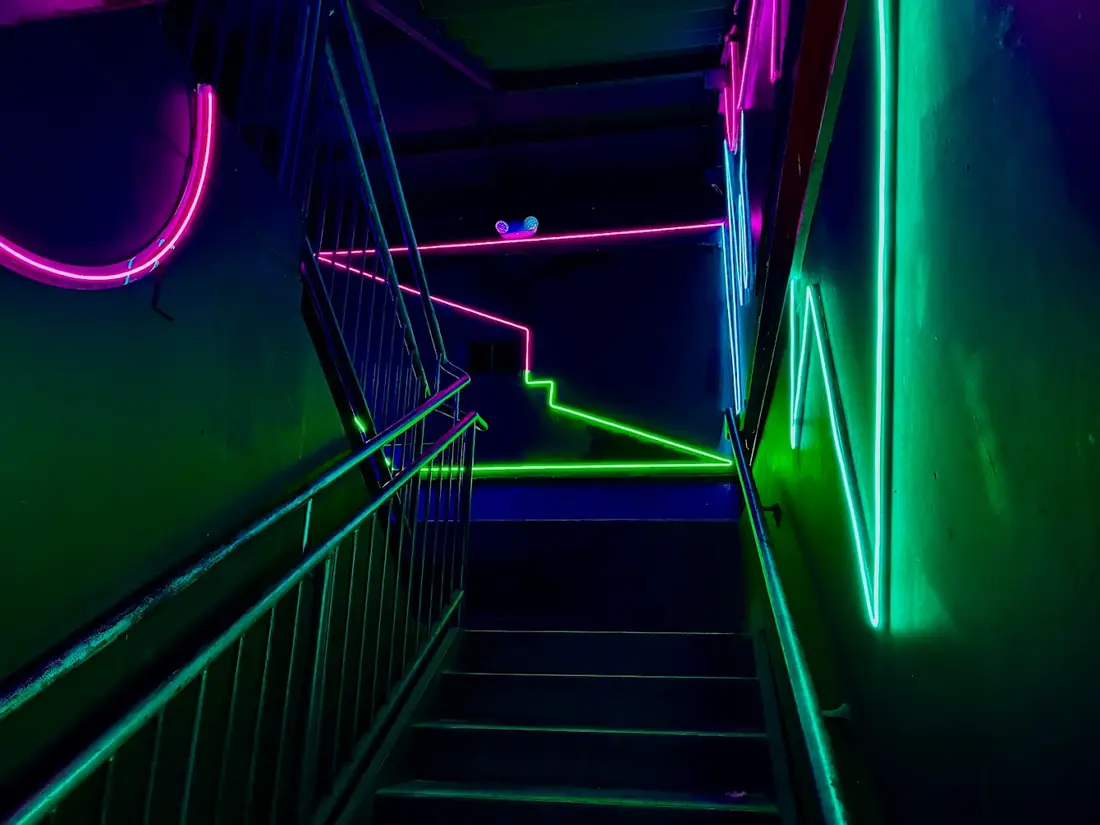 Stairwell lined with pink, green and teal neon tubes leading up to the lounge