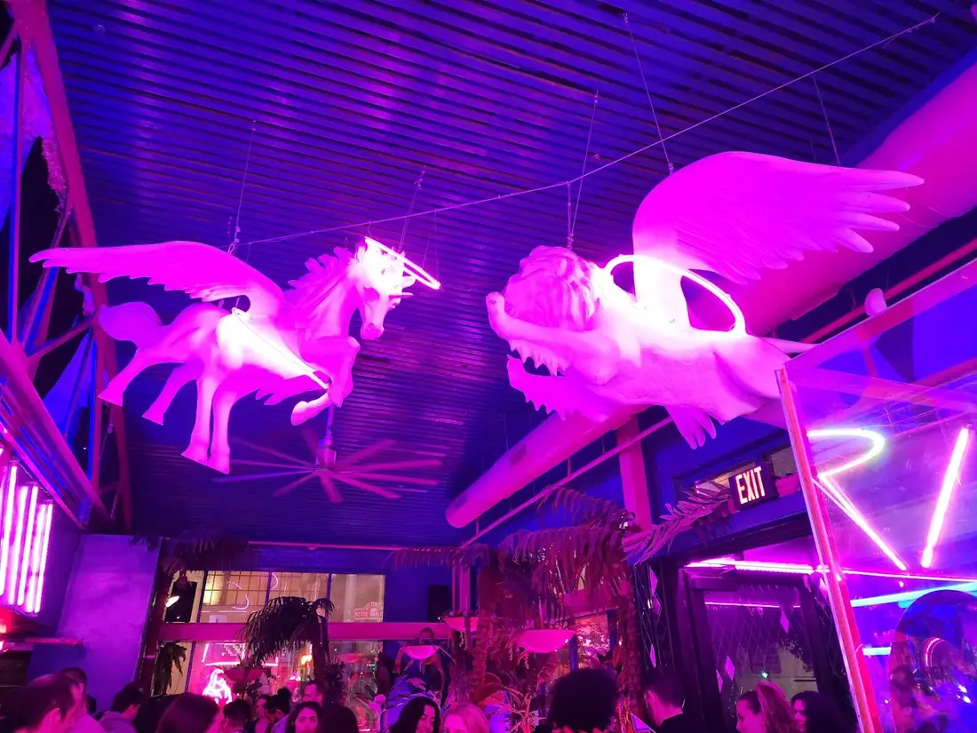 White pegasus and winged lion sculptures with neon halos lit pink over the main room