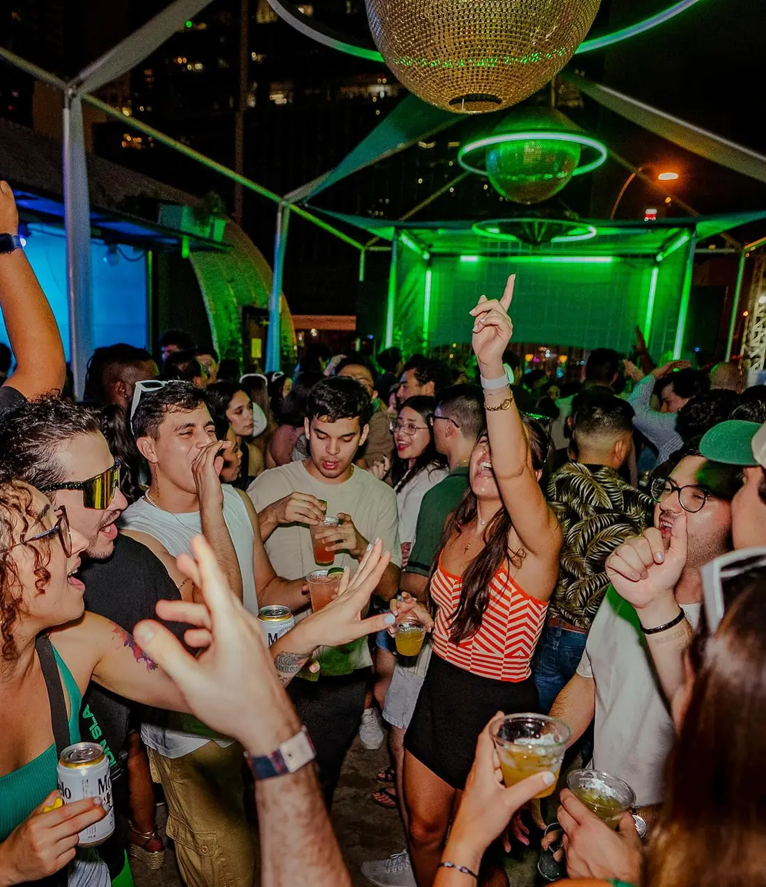 Packed rooftop dance floor under a gold disco ball and green neon rings