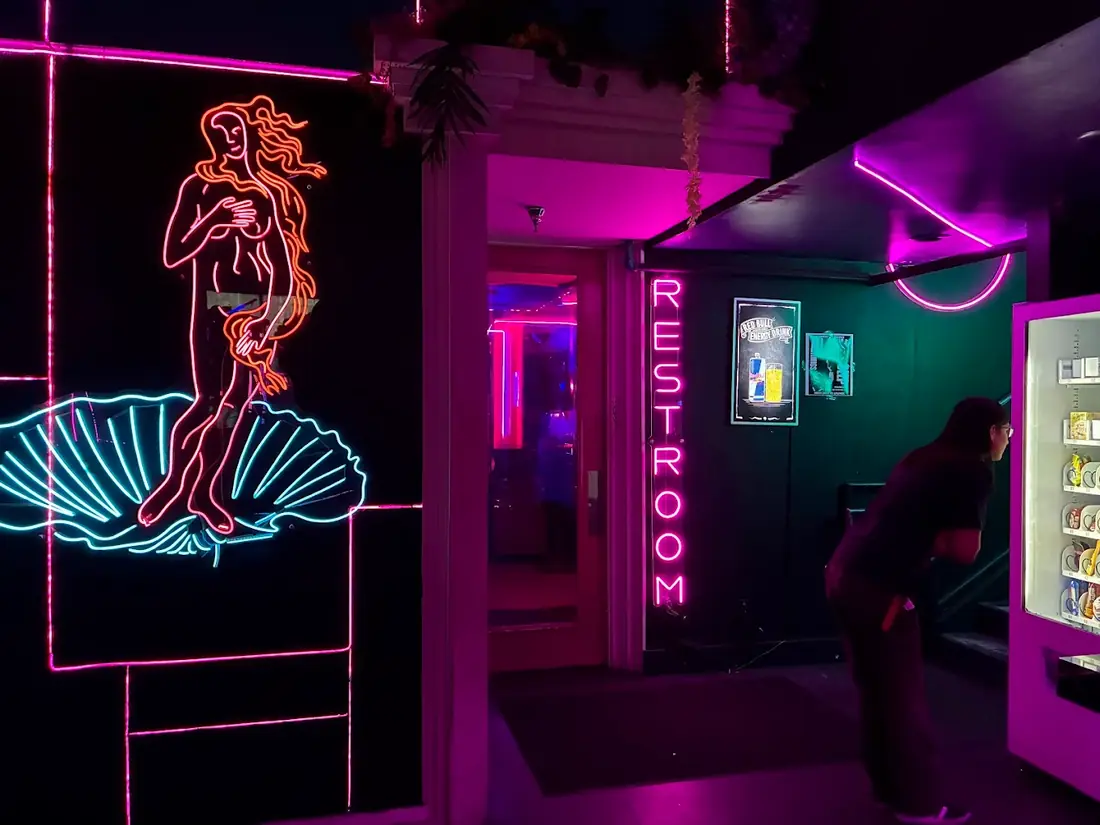 Neon Birth of Venus sign beside a pink neon restroom sign